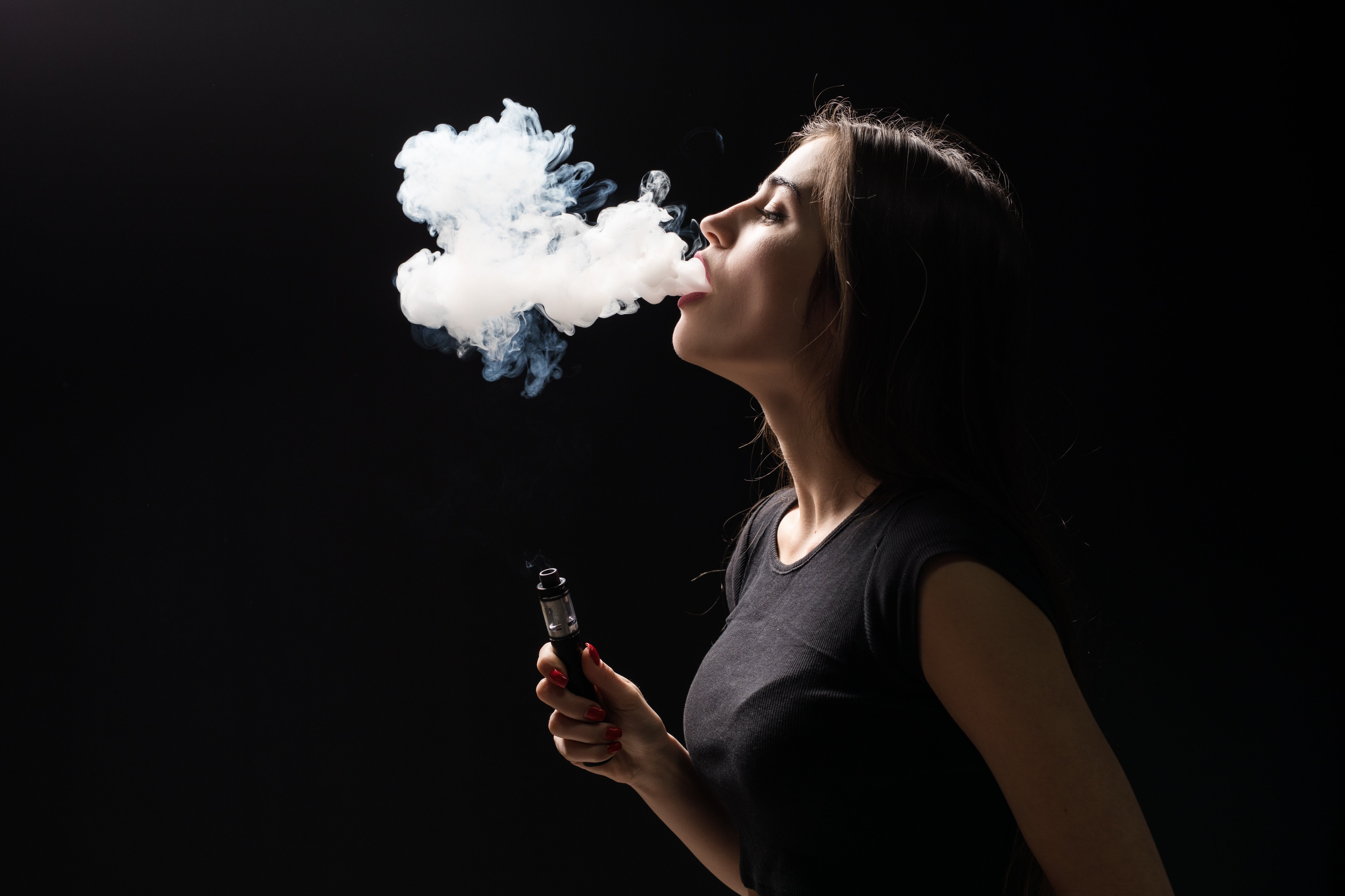 A woman producing large, thick vapor cloud from cannabis vape on black background